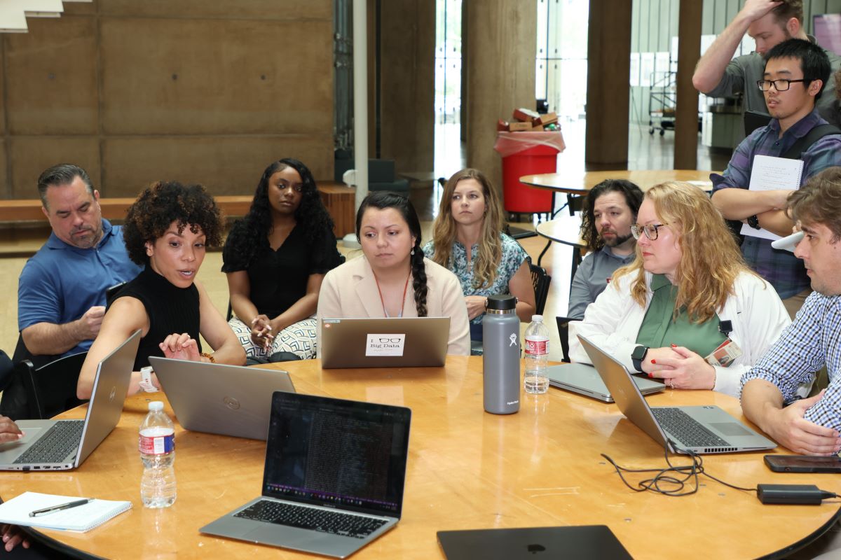 Data Analytics team working at circular table showing data on laptops.