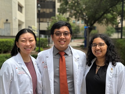 Three students in white coats stand outdoors