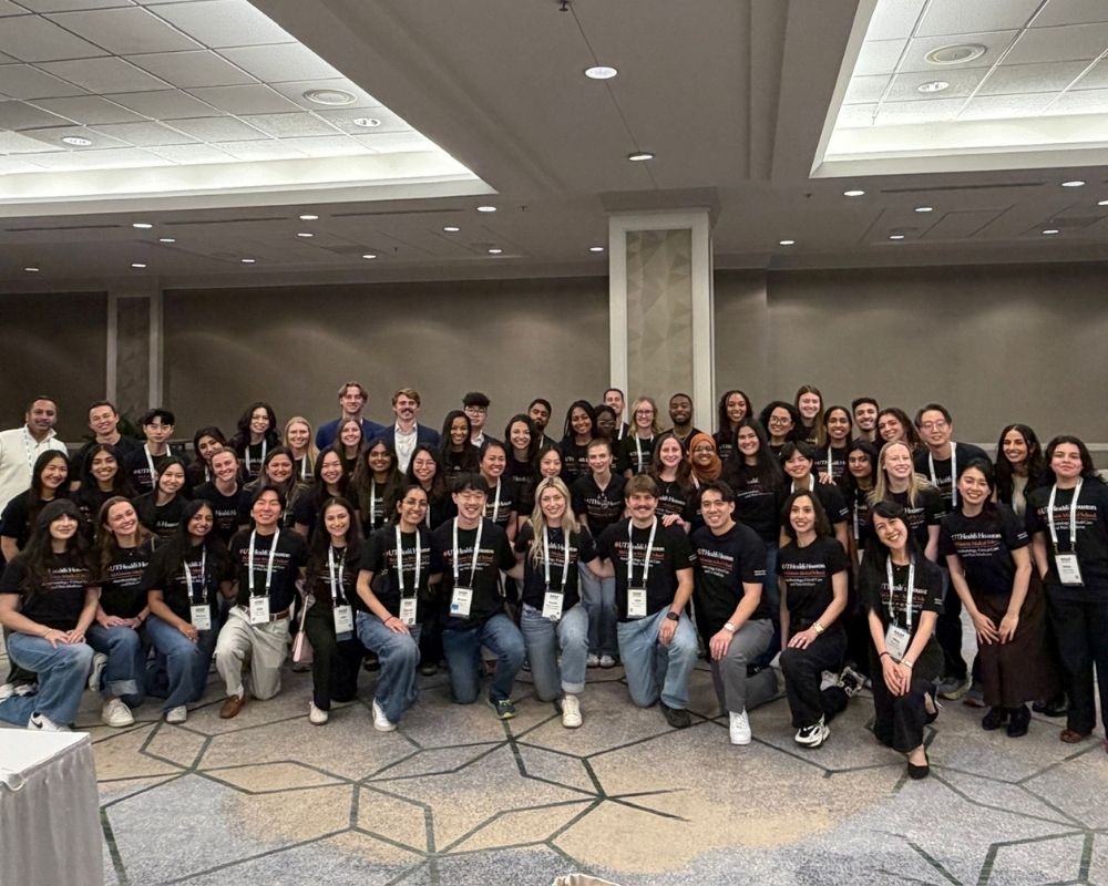 Large group of MSA students and faculty posing together at a conference, wearing matching shirts