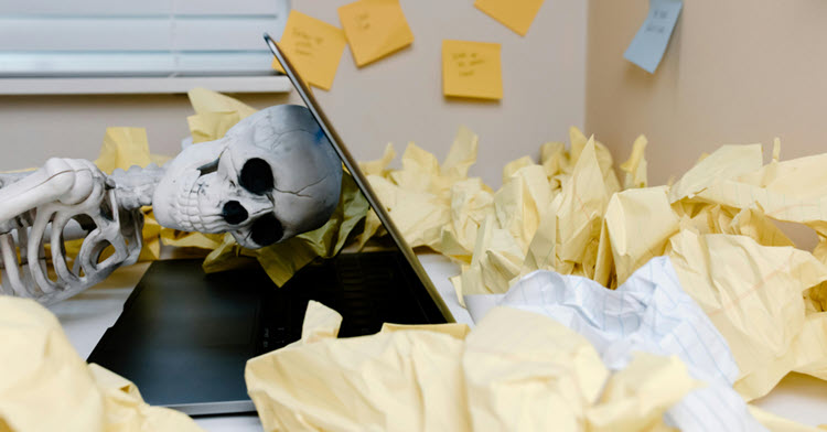 Skeleton on laptop drowning in papers