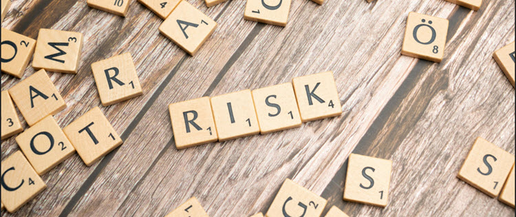Scrabble letter tiles arranged on a wooden surface spelling the word ‘RISK,’ with additional tiles scattered around.