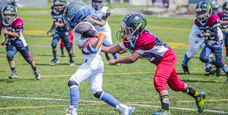 Kids playing football in white uniforms, other team red, white, and blue uniforms.