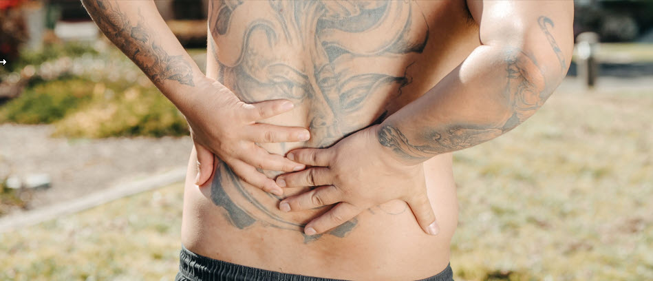 Person with back and arm tattoos grabbing back in pain