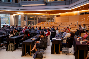 An lecture audience sitting at tables, listening intently