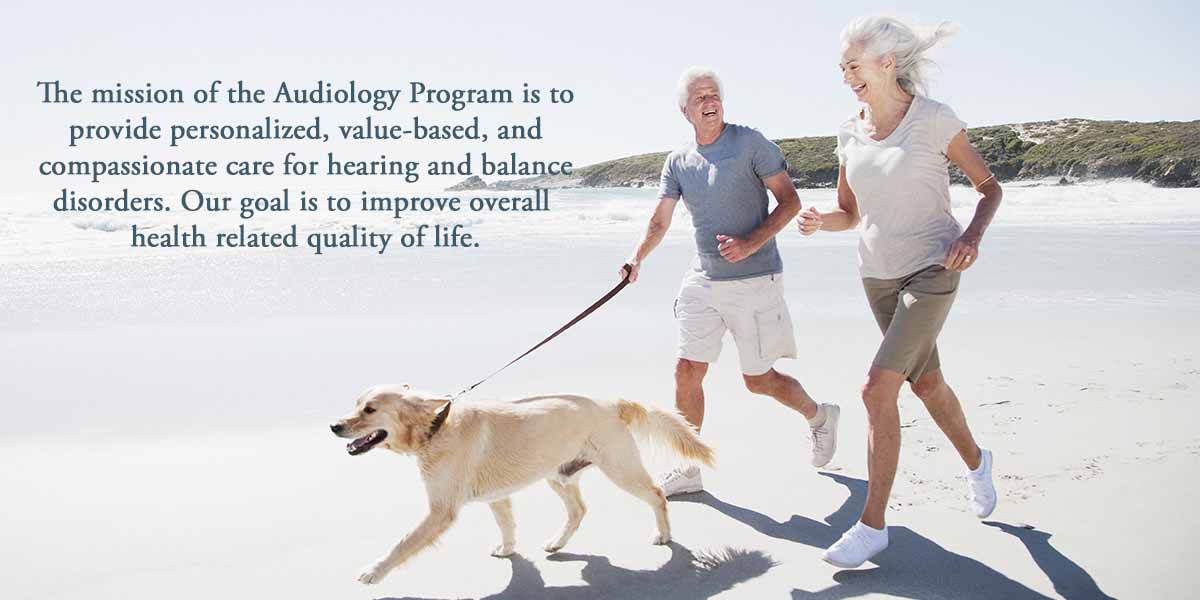 man and woman on beach with dog. Text: The mission of the Audiology Program is to provide personalized, value-based, and compassionate care for hearing and balance disorders. Our goal is to improve overall health related quality of life.