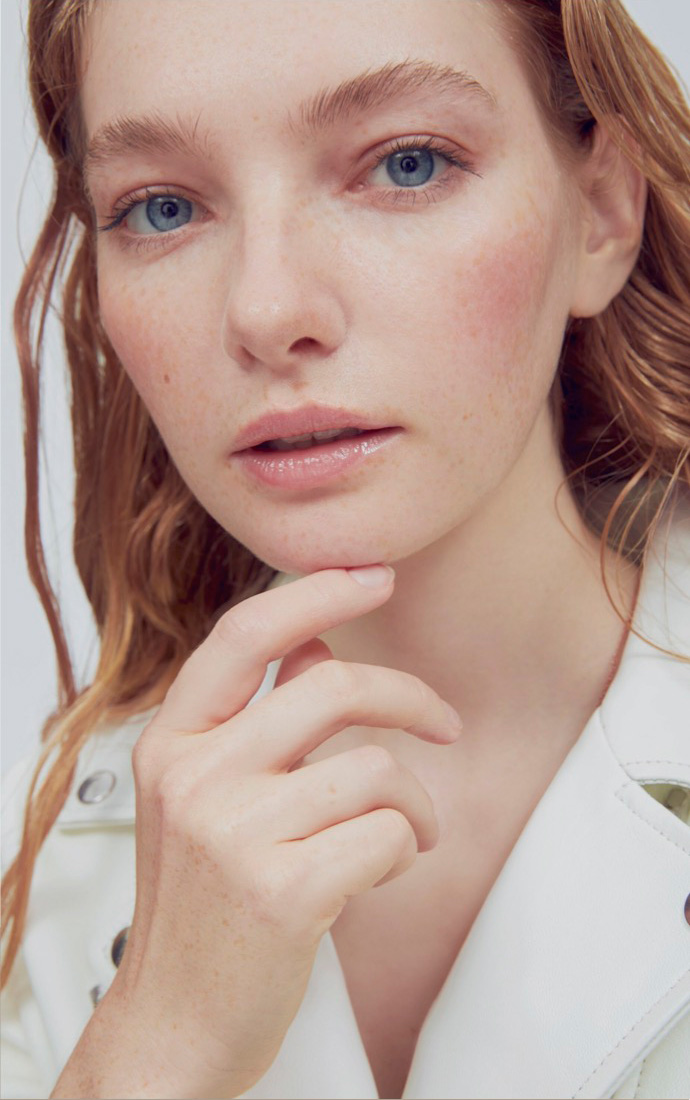 white woman with red hair touching her chin and wearing a white jacket