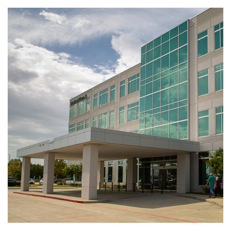 Modern office building with large glass windows and a covered entrance under a partly cloudy sky.