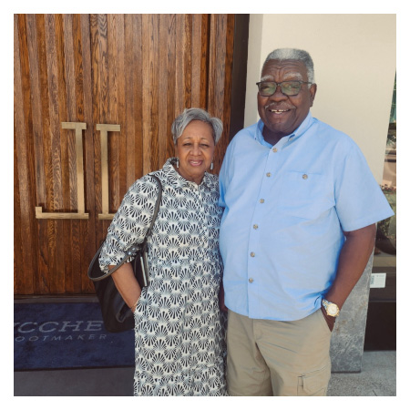 Larvell and Alice Love standing close together outside a wooden door with brass handles, dressed in casual attire.