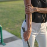Person gripping a golf club with one hand while holding the inner elbow, suggesting pain consistent with golfer’s elbow.