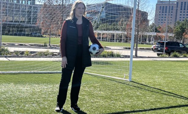 Summer Ott, PsyD, stands on a soccer field holding a soccer ball in front of a goal while discussing concussion awareness and player safety in soccer.
