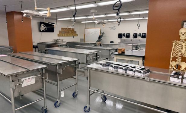 Cadaver laboratory equipped with multiple stainless steel workstations, overhead lighting, and anatomy teaching resources for medical and surgical training programs.