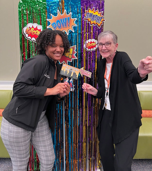 Two GME coordinators pose in front of a photo backdrop.