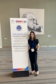 Dr. Perez stands in front of banner at Conference