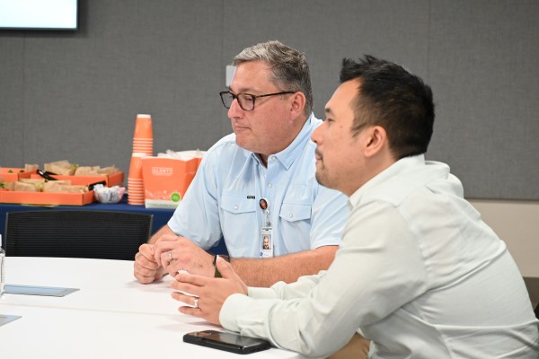 Two men sitting at a table, listening to presenter