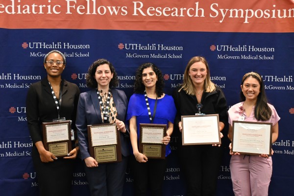 Five female fellows standing in front of banner holding their awards