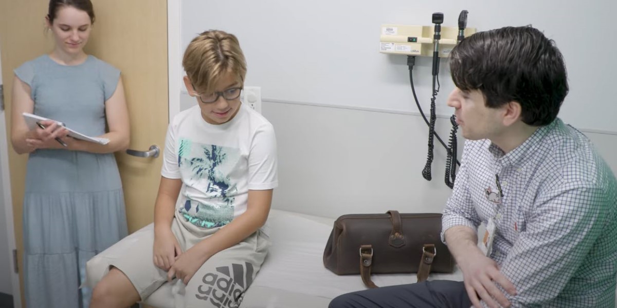 Doctor talks to his young patient in the exam room while resident takes notes