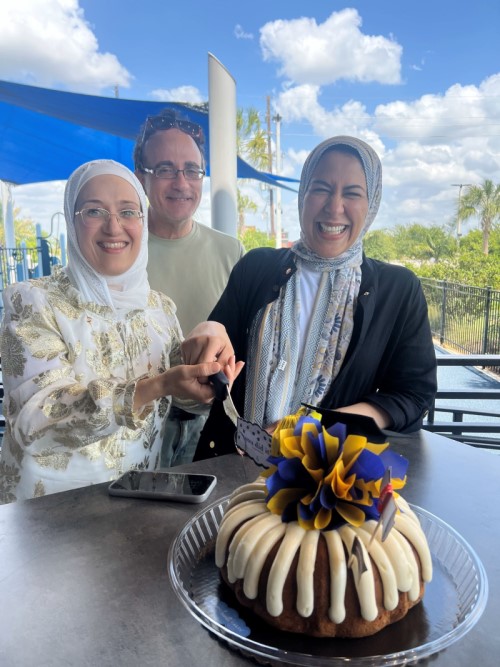 Two women cutting a cake with man in background