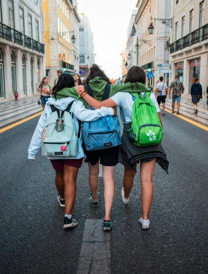 Three girls with backpacks walking down the street, arms around shoulders