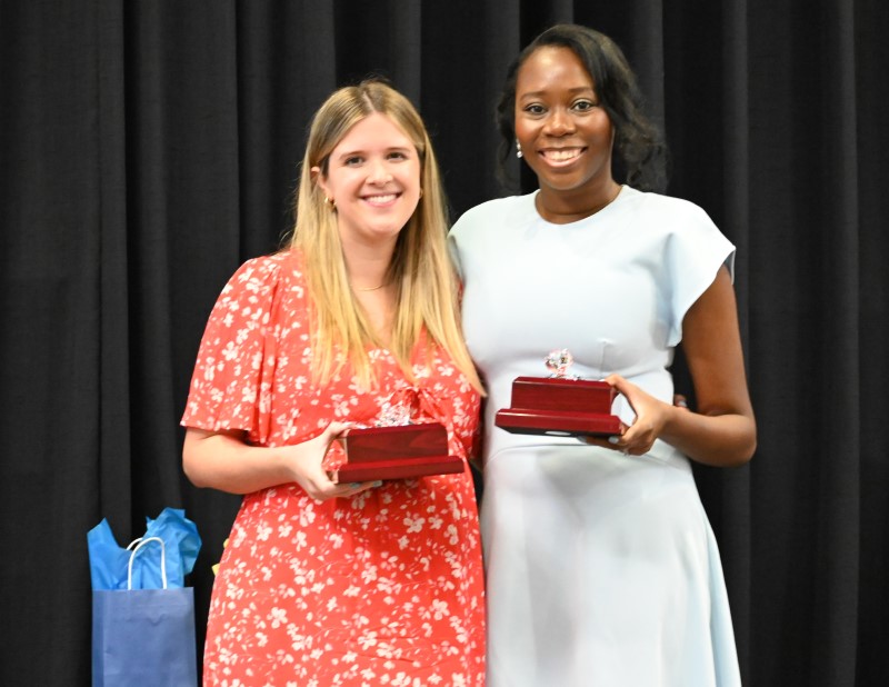 Two women in front of black curtains, holding awards
