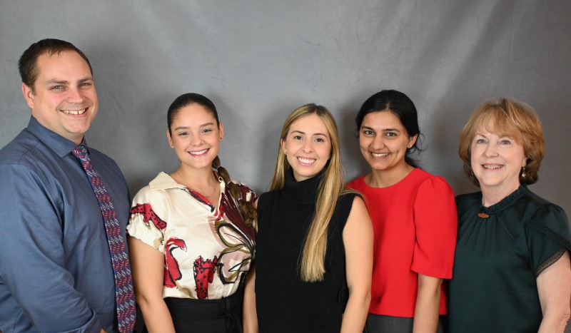 One man and four women poses in front of gray backdrop