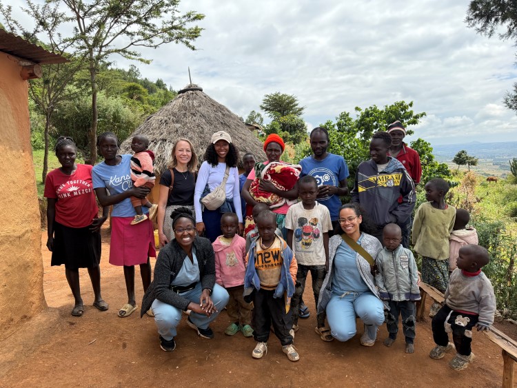 A group of people standing on red clay outside a house