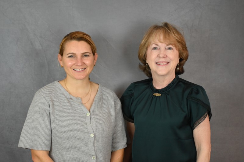 Two women standing side by side in front of a gray backdrop