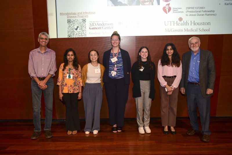 Group of 7 people standing on a stage in front of PPT screen