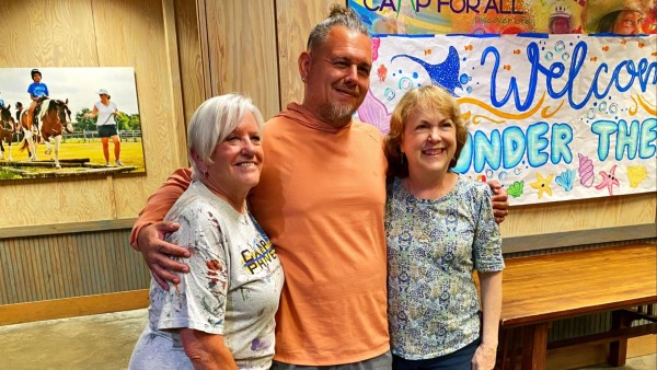Man with arms around two women, all smiling