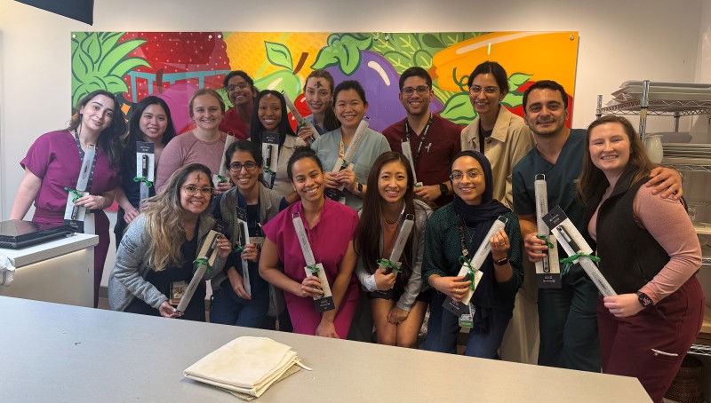 Group of young people pose with kitchen utensils in front of brightly colored mural in kitchen