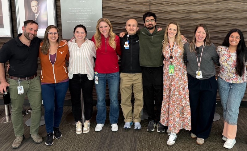 Group of people standing together in a lobby with their arms around each other's shoulders