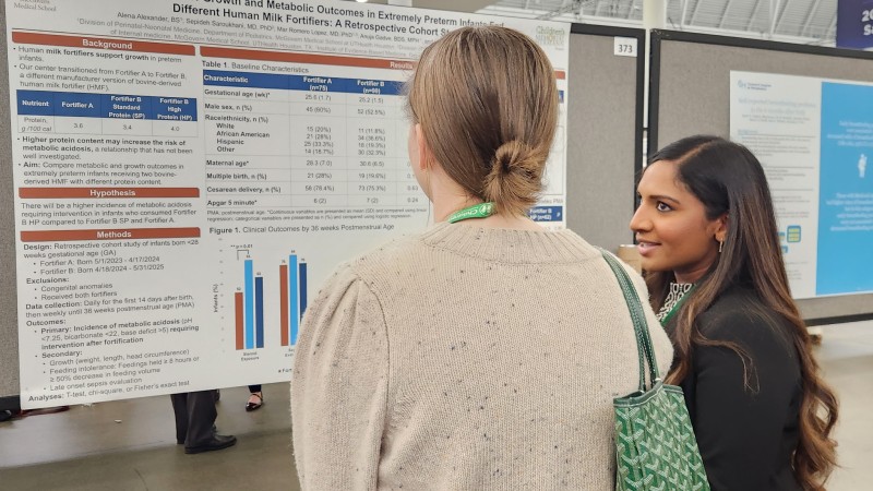 Two women discussing research in front of poster