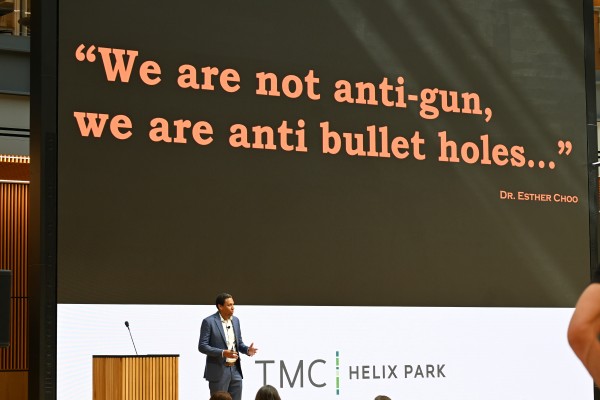 Dr. Dark standing in front of screen that reads, "We are not anti-gun, we are anti bullet holes ..."