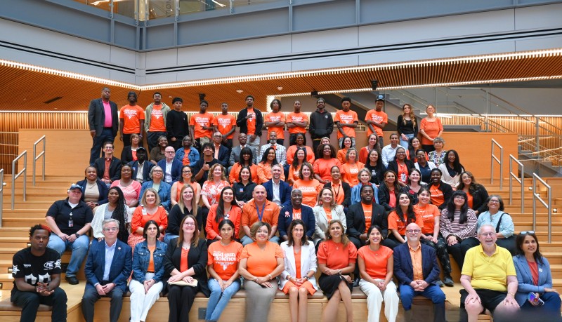 Large group of people, many wearing bright orange, on steps in conference center