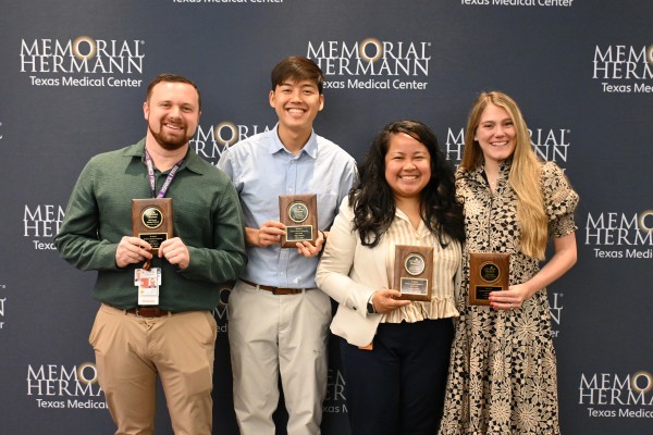 Four people in front of banner holding plaques