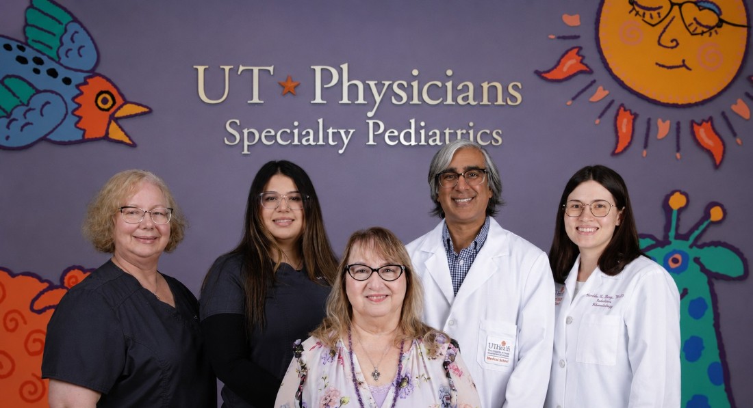 Five people, 2 in white coats, smiling in front of UT Physicians sign