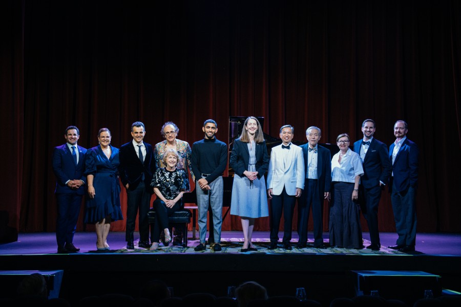 Group of well-dressed people standing on stage with a grand piano behind them