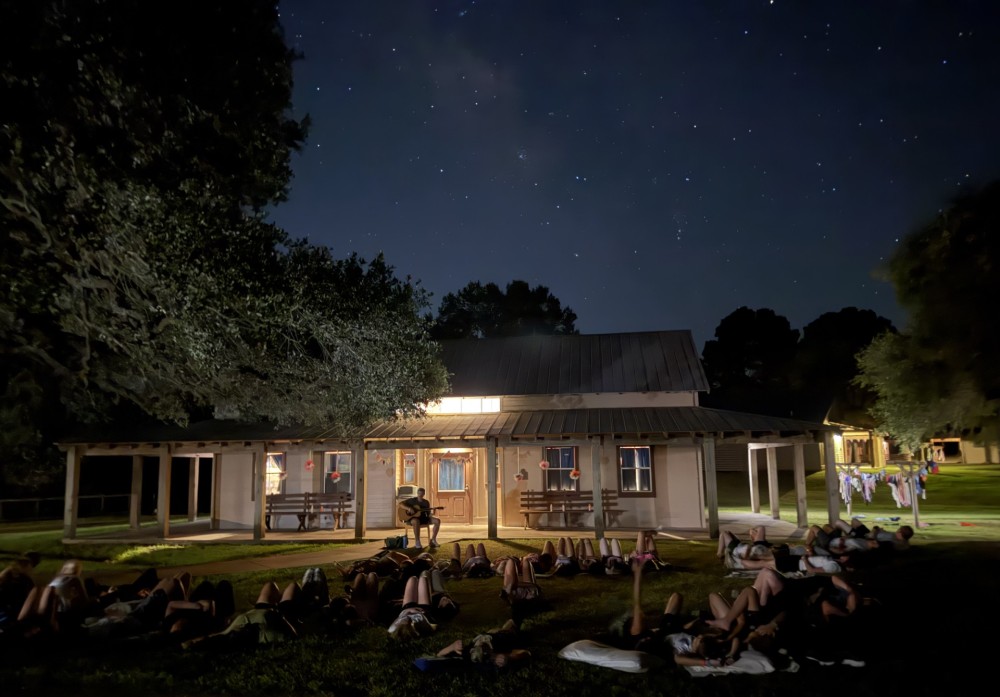 Campers laying out under a big starry sky while man plays guitar