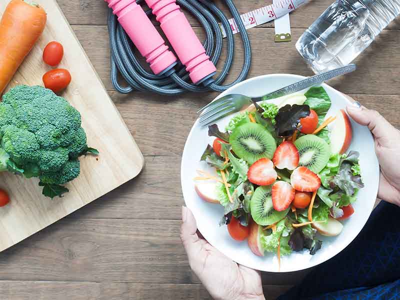Picture of a table with a bowl of fruits and veggies, water, and a jump rope