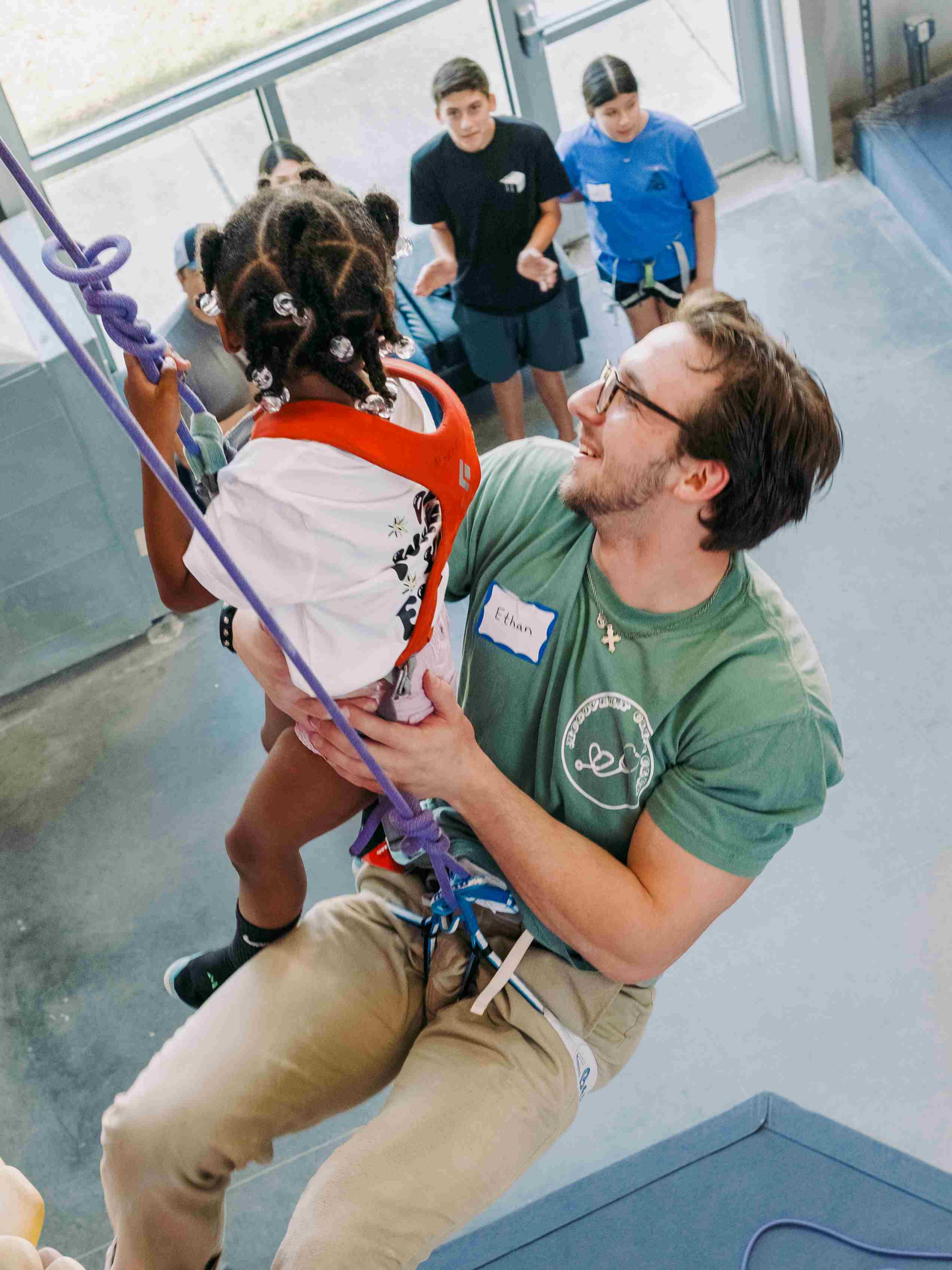 students of Climbing Club helping kid climb wall.