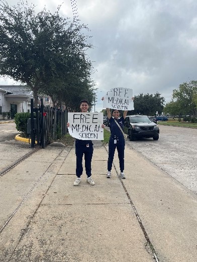 student volunteers holding signs up outside health fair venue about free medical screenings.