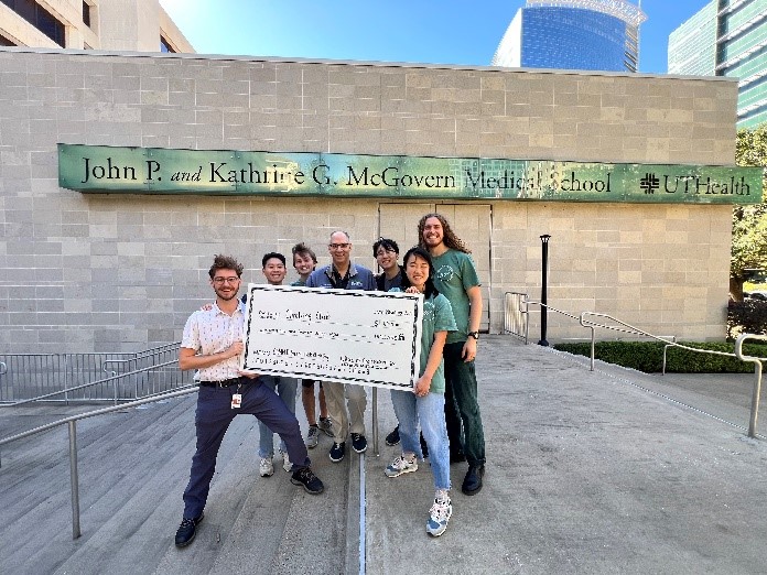 group photo of students apart of the Climbing Club holding up a check outside McGovern Medical School with the amount they were granted.