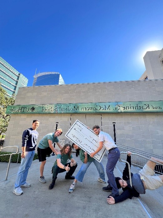 another group photo of students apart of the Climbing Club holding up a check outside McGovern Medical School with the amount they were granted.