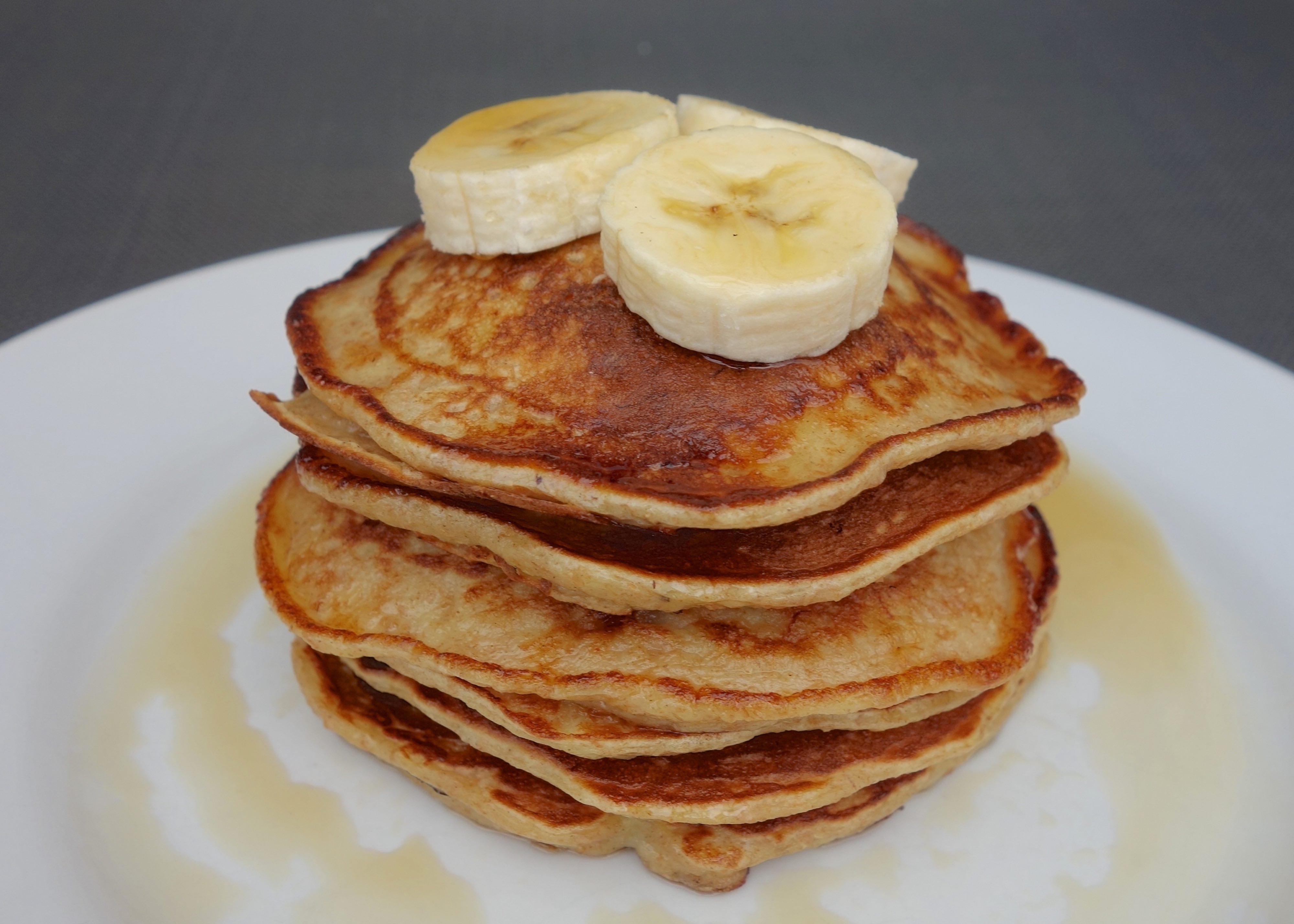 Stack of banana oat pancakes topped with banana slices and a maple syrup drizzle
