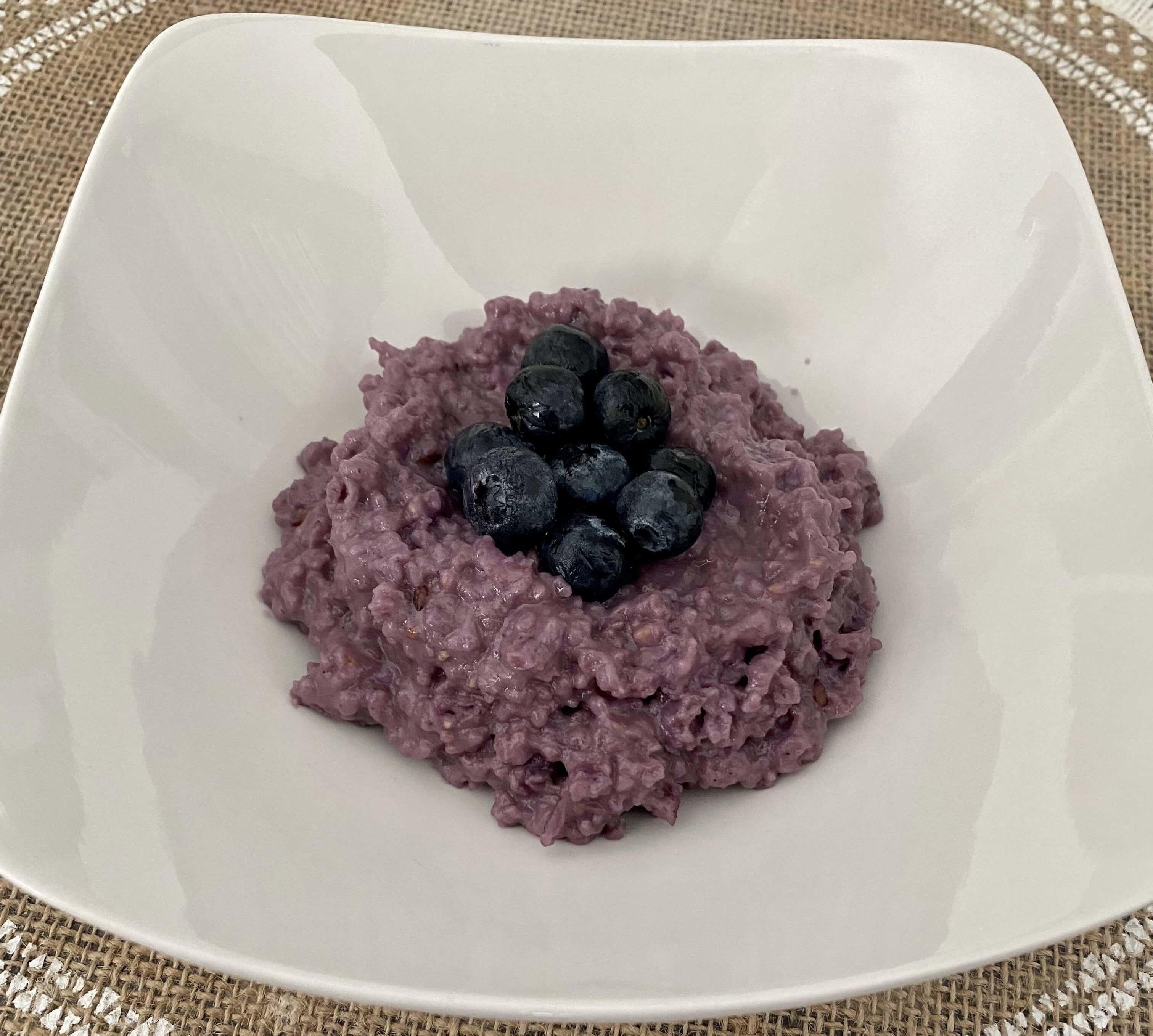 Purple berry oatmeal topped with blueberries on a white plate