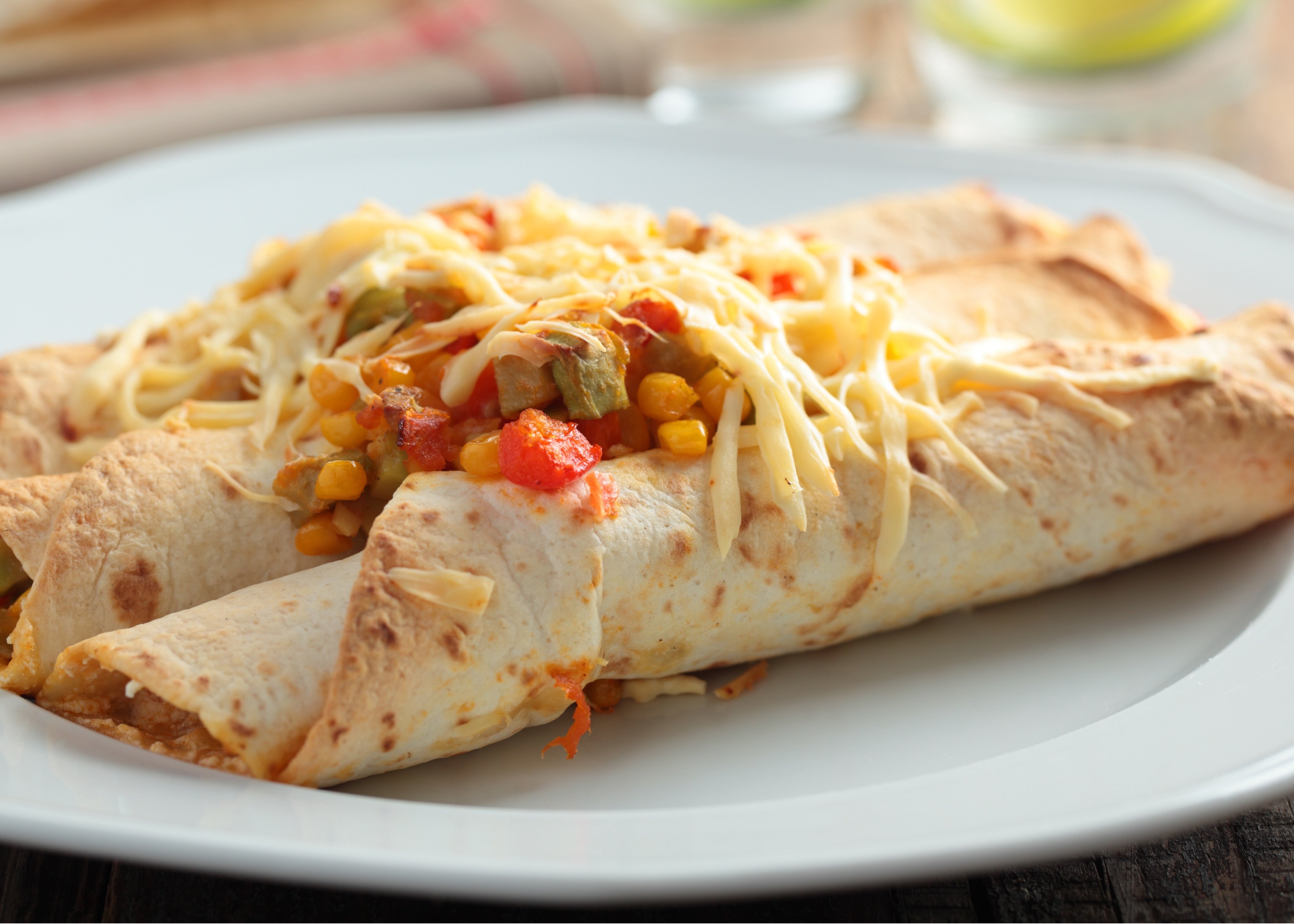 Three spinach and bean enchiladas topped with salsa and shredded cheese