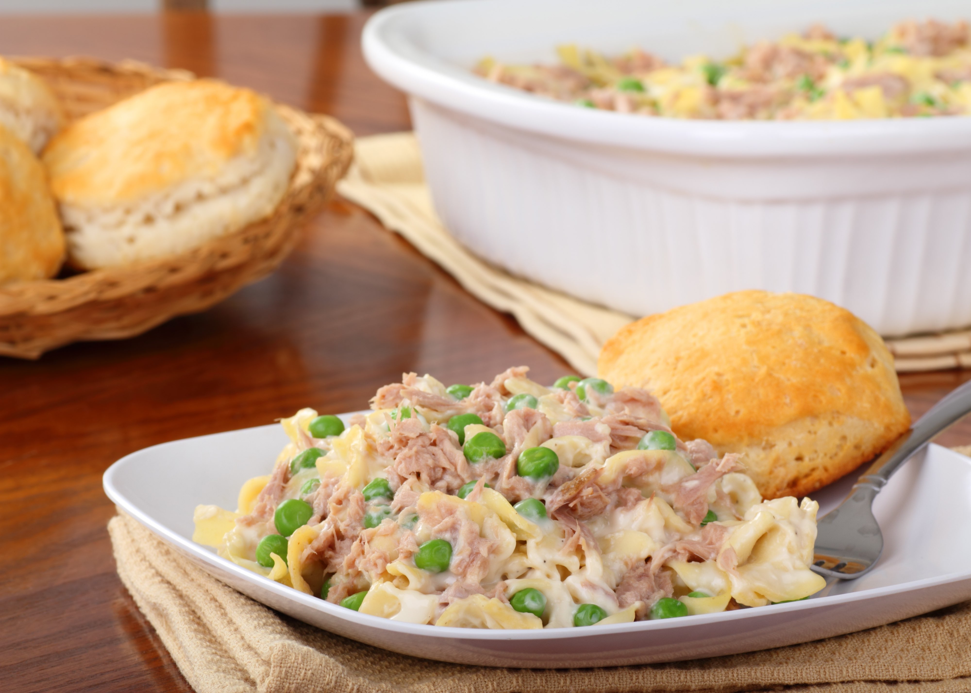 Tuna noodle casserole with a roll on a white plate