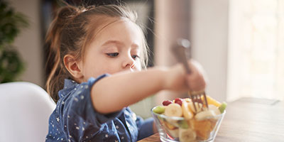 child eating fruit from a glass bowl