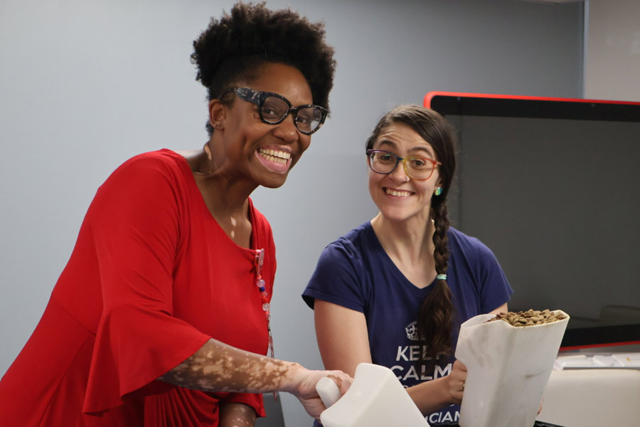 Two smiling volunteers scoop dry pet food into bags at a table during an AniMeals packing event.