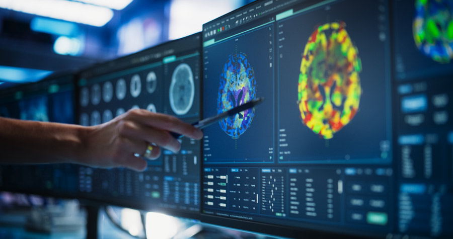 A scientist looks at and points to a colorful image of the brain on a computer screen