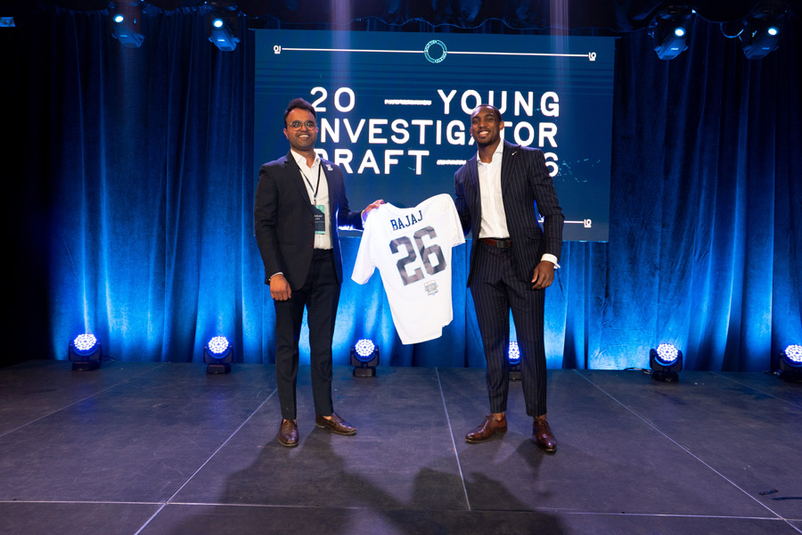 Dr. Sunanjay Bajaj receives a jersey that reads Bajaj 26 from another man dressed in a suit as the 2026 Young Investigator Draft.